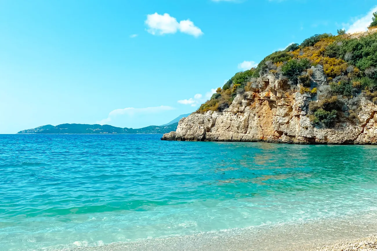Turquoise water and a white pebble beach below a rocky headland on the coast near Kaş